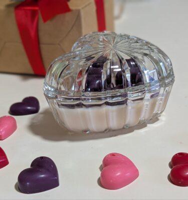 Candle in heart shape glass bowl with wax hearts on top.