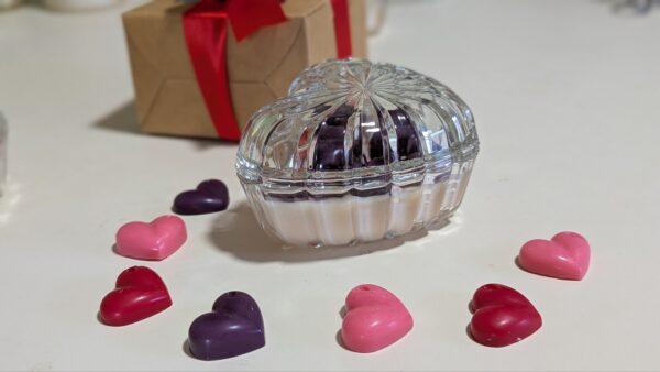 Candle in heart shape glass bowl with wax hearts on top.